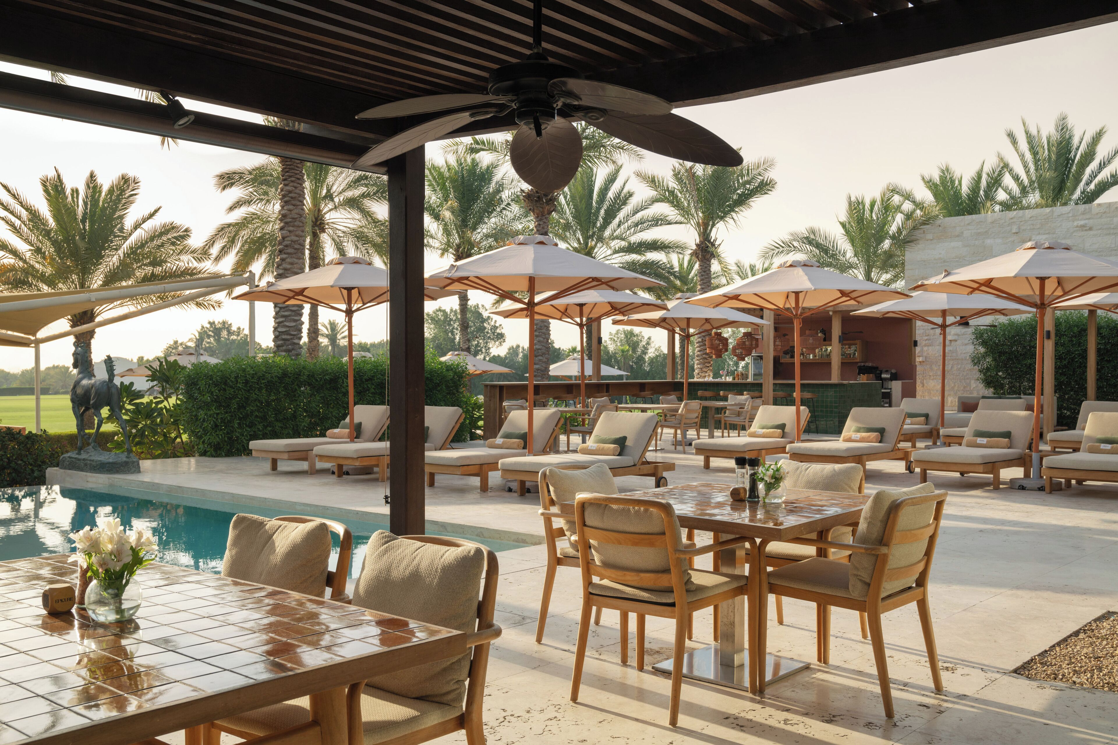 An outdoor seating area with tables and chairs, umbrellas, and a pool.