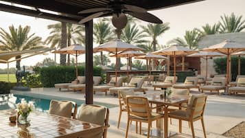 An outdoor seating area with tables and chairs, umbrellas, and a pool.