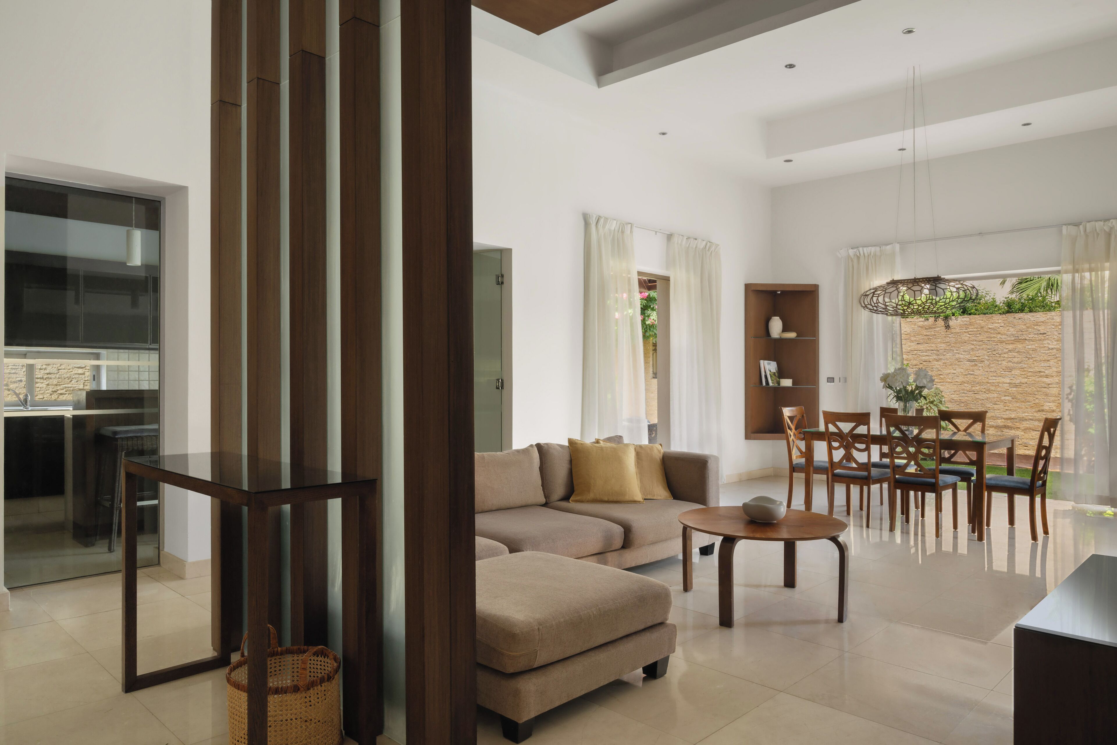 A modern living room with a sectional sofa, a glass coffee table, and a dining area with wooden chairs and a table.