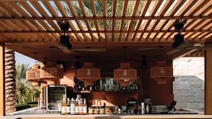 A bar area with a wooden pergola, green tiled bar counter, and three stools.