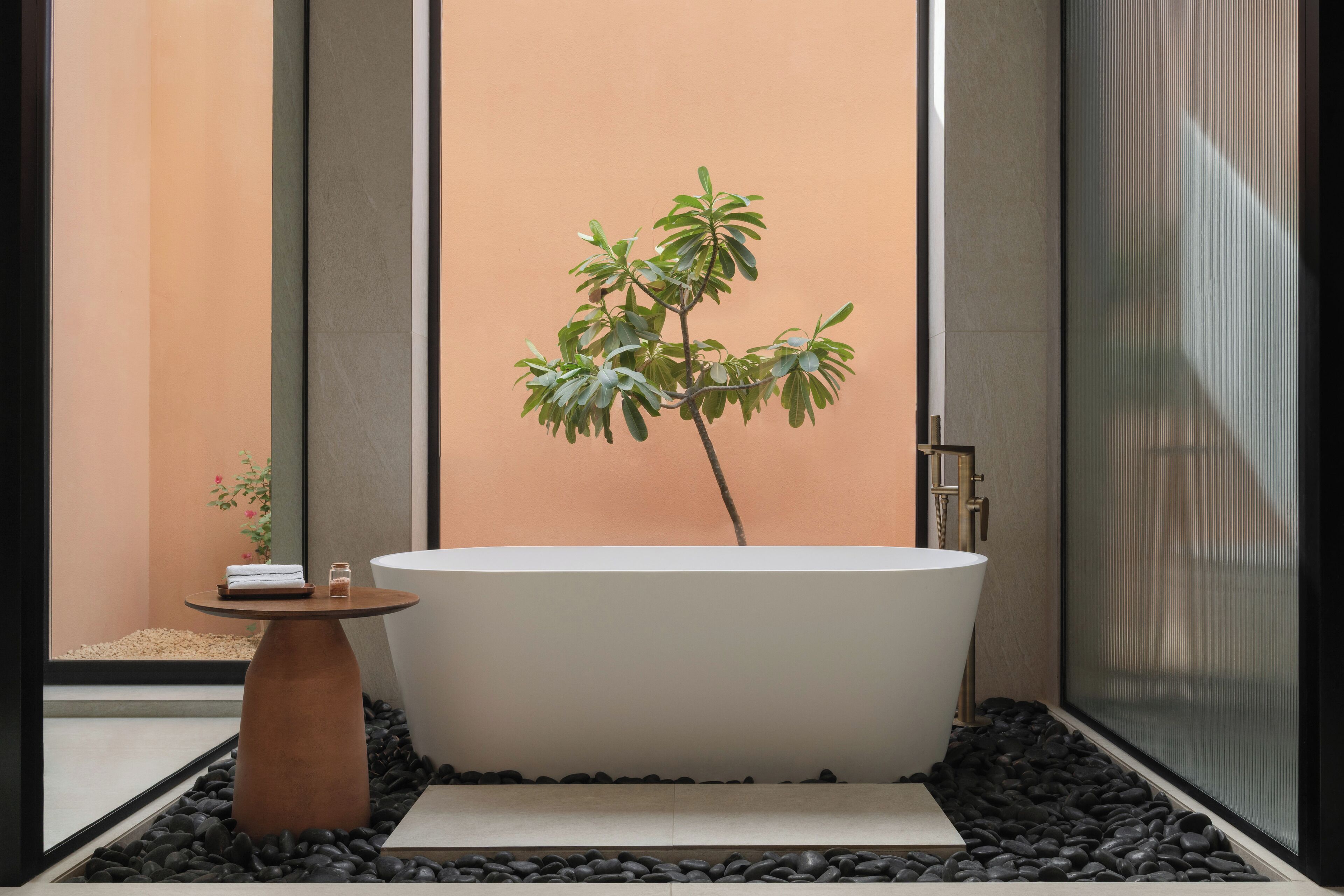 Un baño moderno con una bañera independiente, una mesita con una toalla y una planta en maceta.