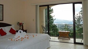 A hotel room with a bed, a chair, a small table, and a balcony with a view. - La Catalina Hotel and Suites (Jesús)