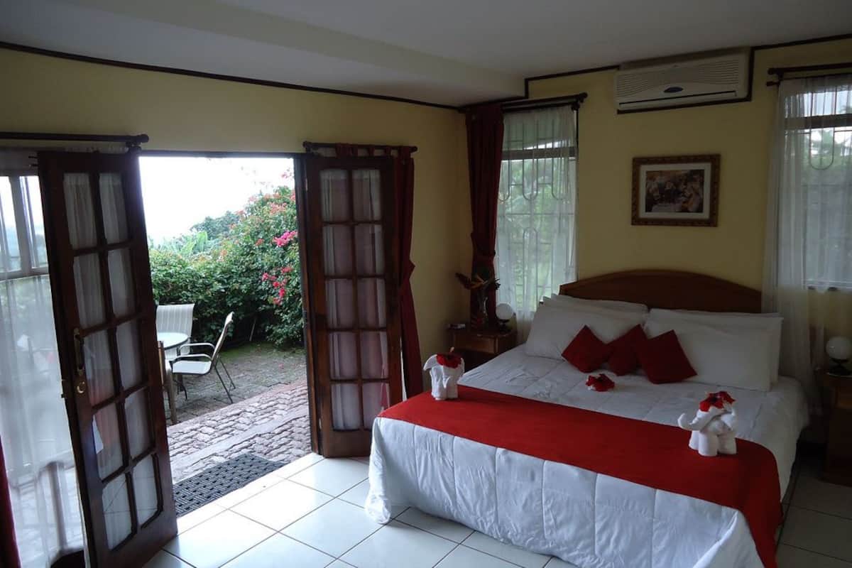 A bedroom with a bed, a nightstand, a window with curtains, and a door leading to an outdoor area.