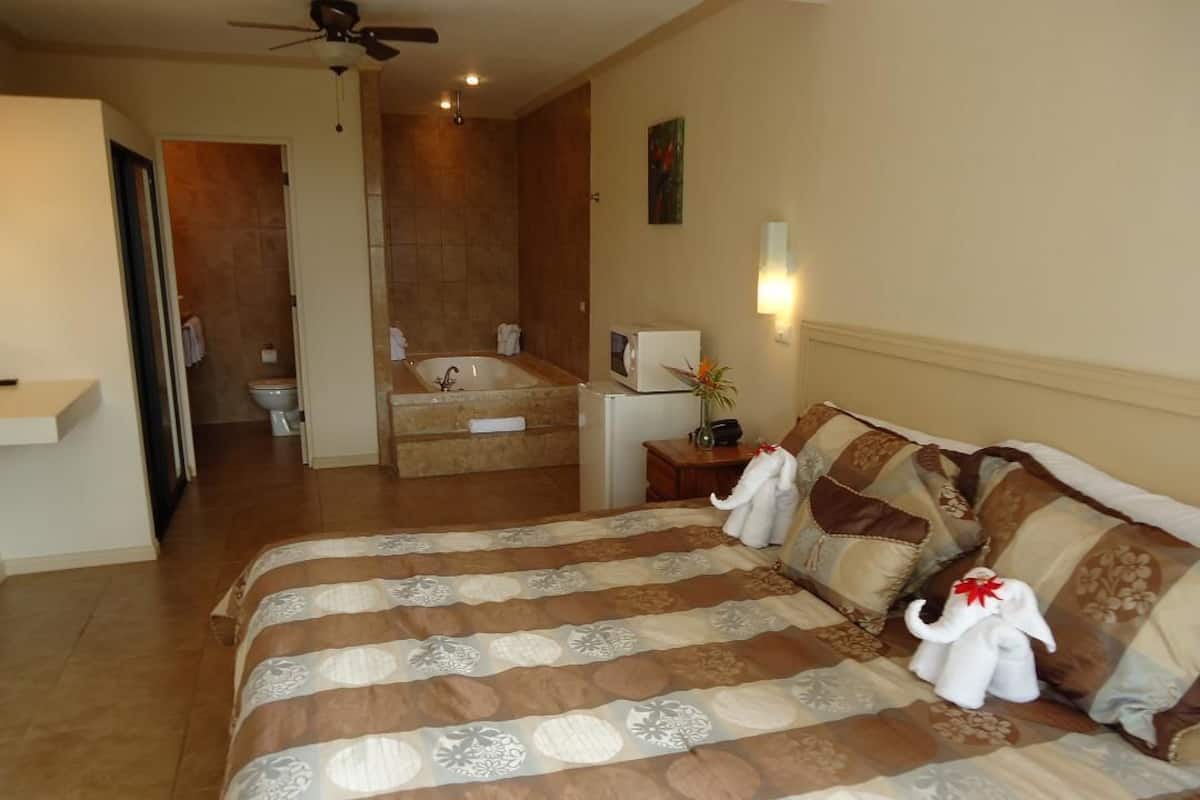A hotel room with a large bed, a bathroom with a bathtub, and a ceiling fan.