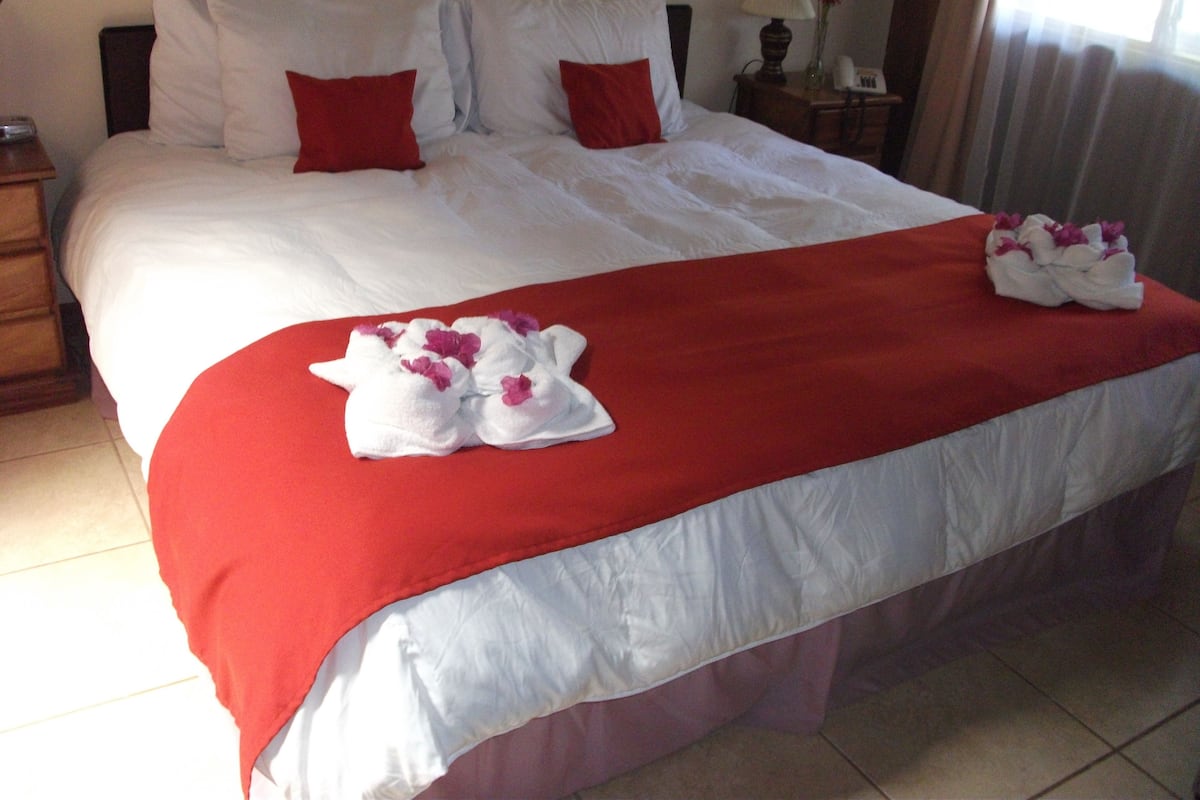 A neatly made bed with white linens, red pillows, and a red bedspread.