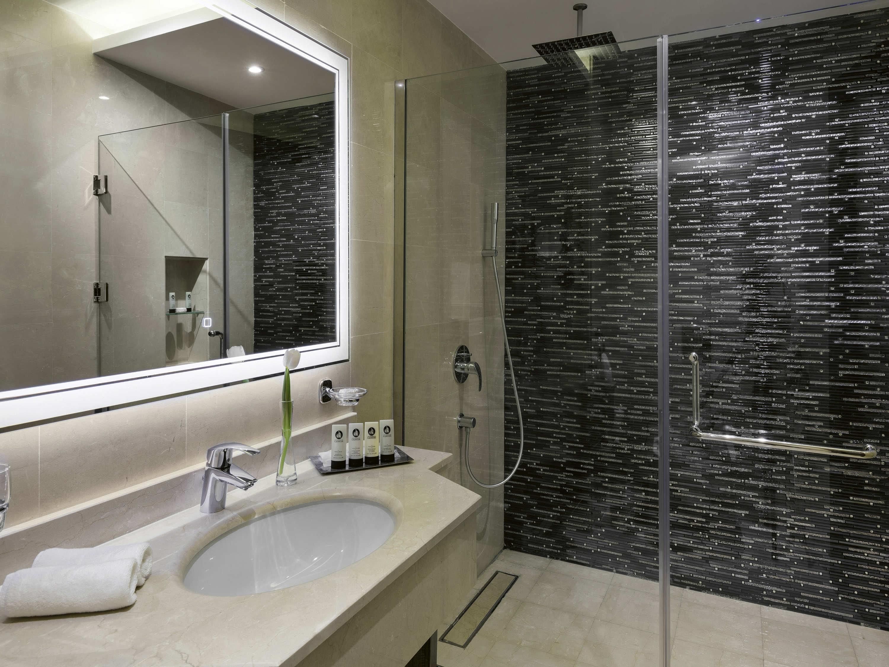 Une salle de bain moderne avec un grand miroir, un lavabo et une douche à parois de verre.