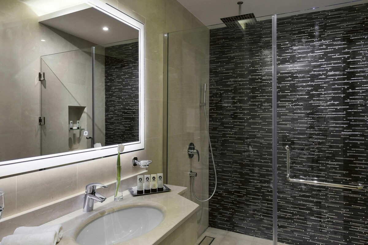 A modern bathroom with a large mirror, a sink, and a glass-enclosed shower.