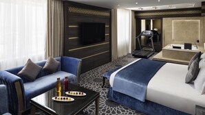 A hotel room with a bed, a sofa, a TV, a treadmill, and a bathroom with a bathtub and shower. - Mövenpick Hotel Qassim (Buraydah)