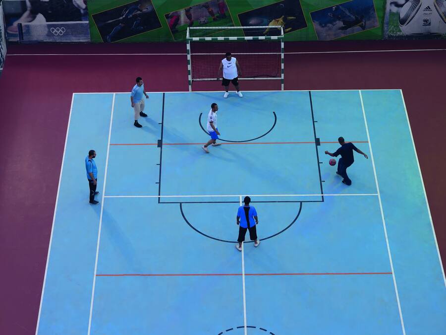 Una cancha deportiva interior con superficie azul, una red y un poste de portería.