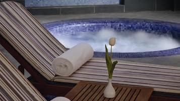 A spa area with a hot tub, striped lounge chairs, and a wooden table with a vase and a candle.