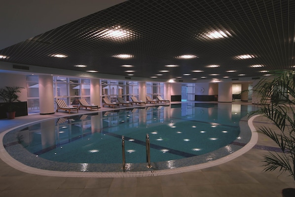 An indoor swimming pool with clear water, surrounded by lounge chairs and potted plants. - Mövenpick Hotel Qassim (Buraydah)