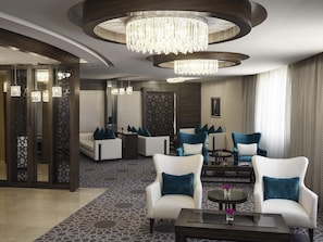 A modern hotel lobby with a chandelier, white sofas with blue cushions, and a patterned carpet. - Mövenpick Hotel Qassim (Buraydah)