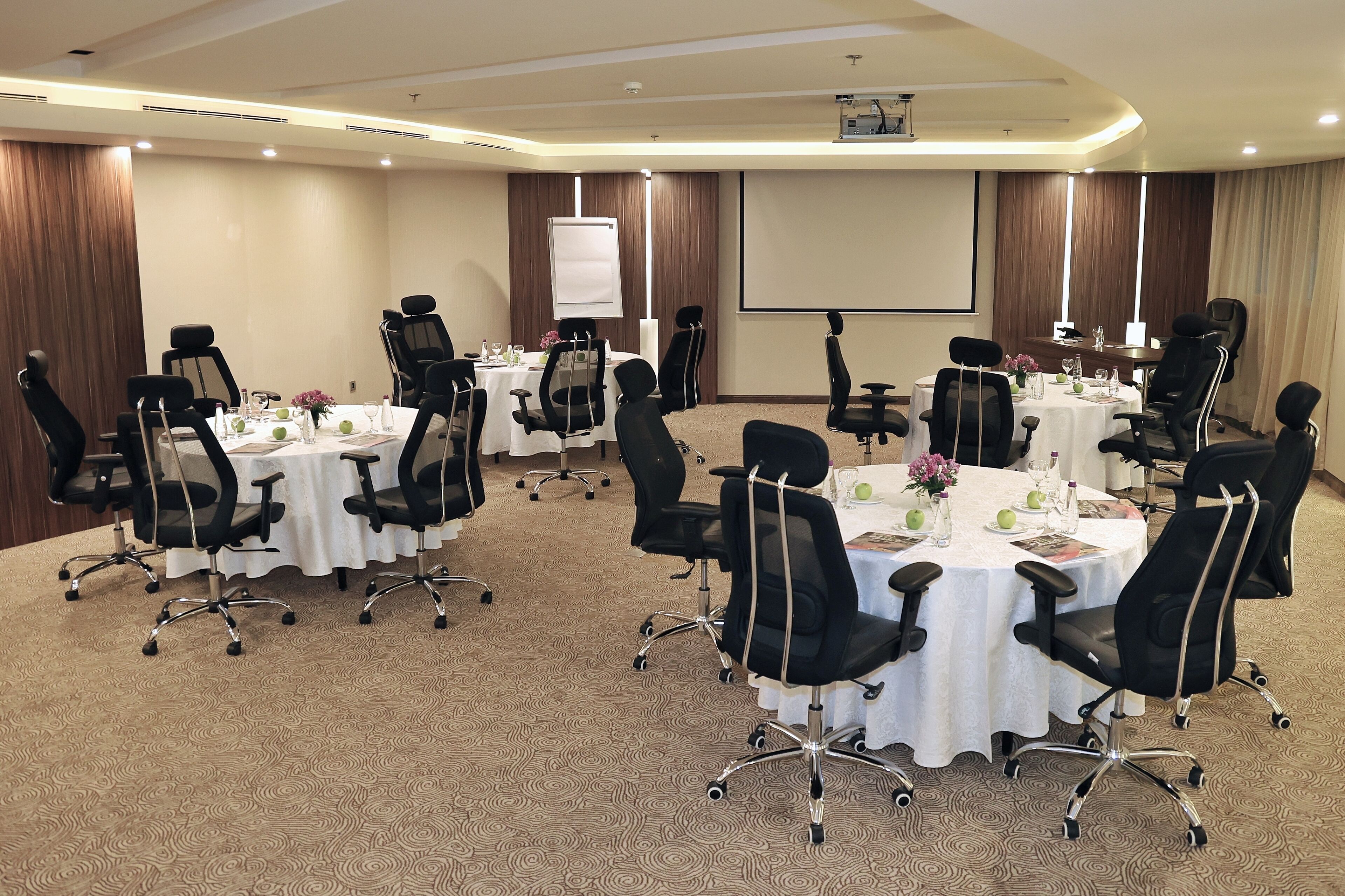 A conference room with multiple tables, black chairs, and a projector screen.
