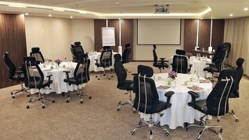 A conference room with multiple tables, black chairs, and a projector screen.
