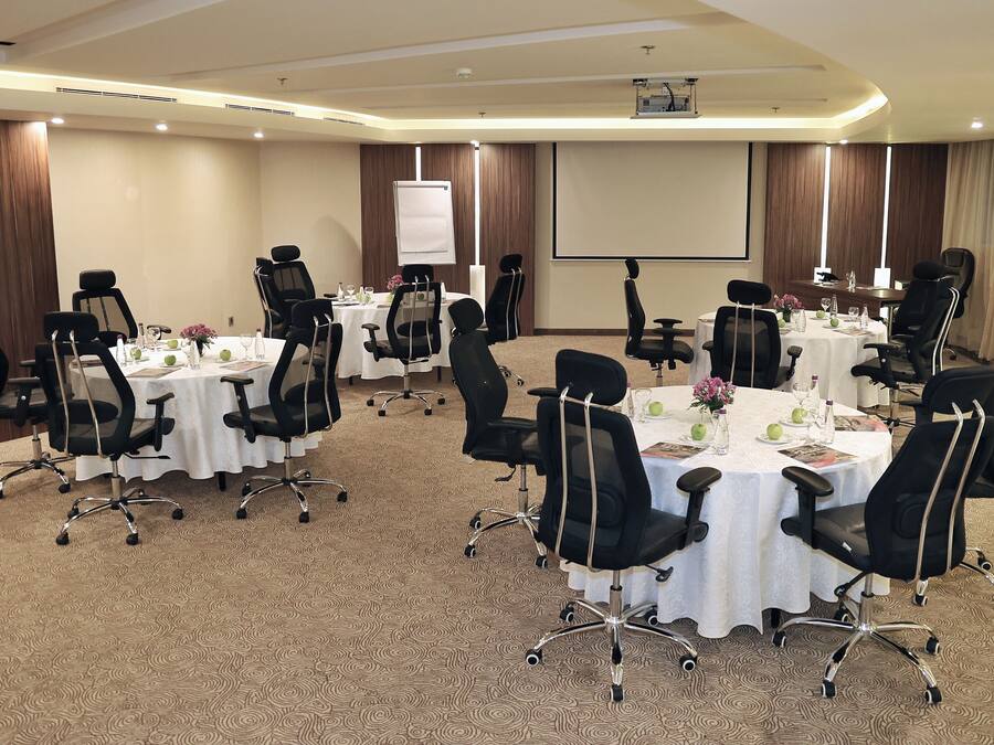A conference room with multiple tables, black chairs, and a projector screen.