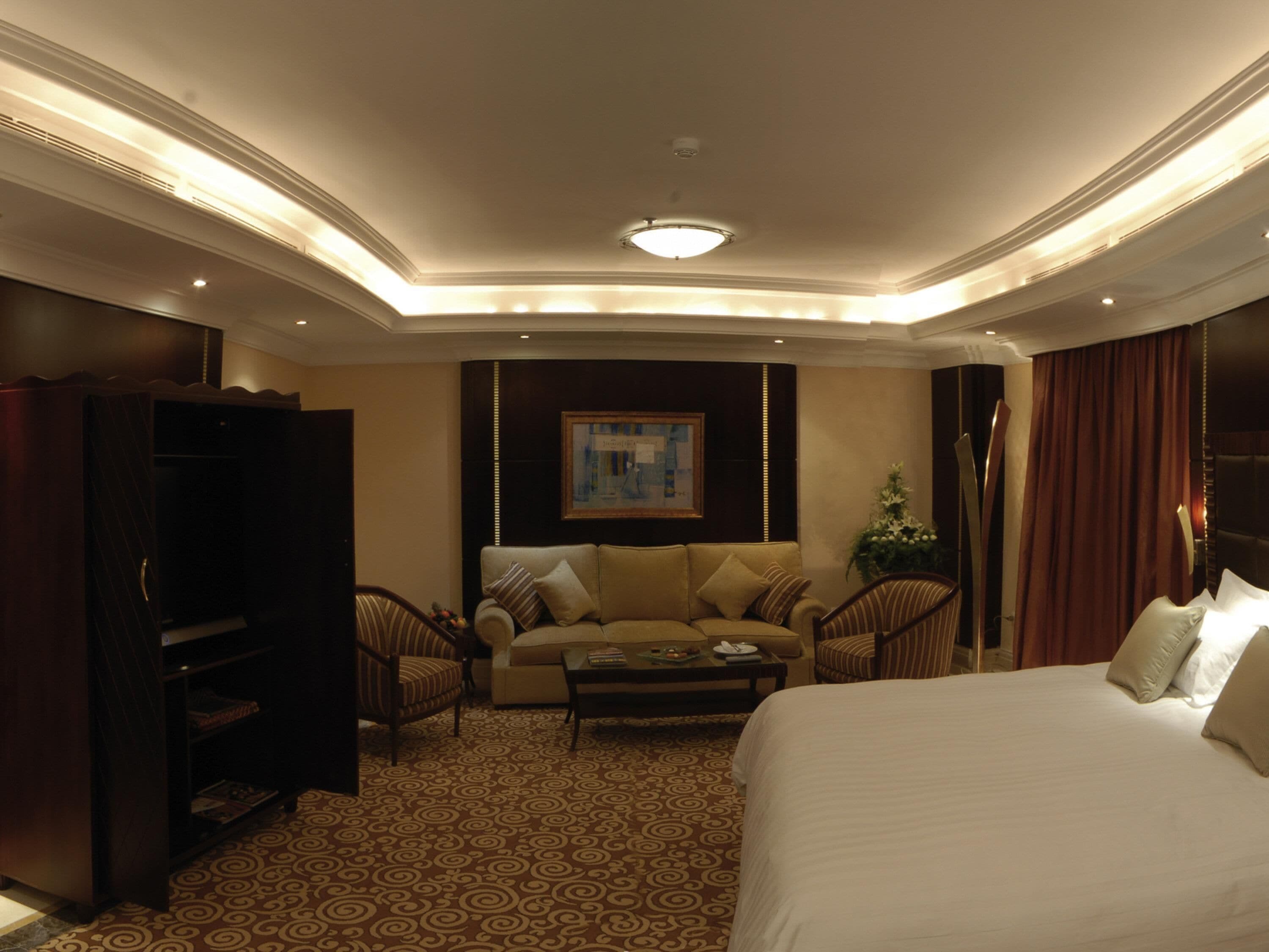 A hotel room with a bed, a sofa, a coffee table, a TV, and a wardrobe.