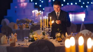 Un homme en costume allume des bougies sur une table dressée pour un dîner formel.