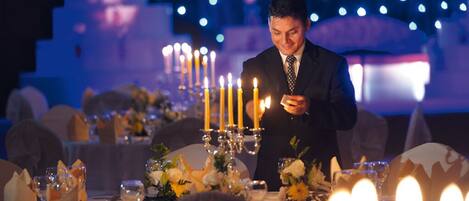 Un hombre con traje encendiendo velas en una mesa dispuesta para una cena formal.