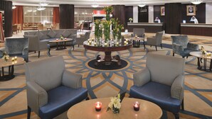 Un hall d’hôtel comprenant des espaces aménagés avec des sièges, un comptoir d’accueil et une table décorative centrale.