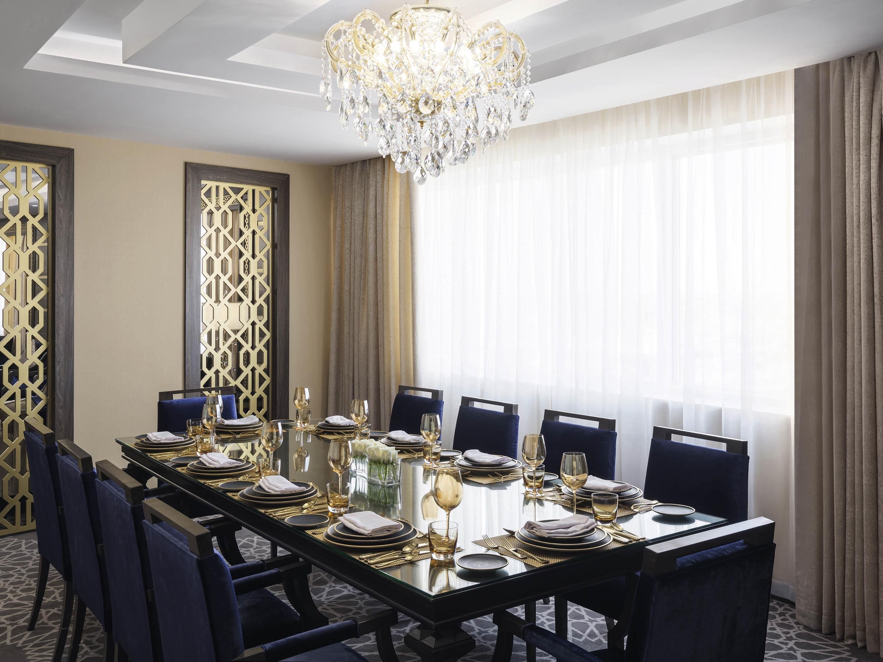 Un comedor formal con una larga mesa dispuesta para ocho personas, un candelabro y vistas a través de cortinas translúcidas.