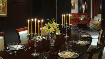 Un comedor formal con una larga mesa dispuesta para una comida, que presenta un candelabro con velas encendidas, un jarrón de flores y un cuadro en la pared.