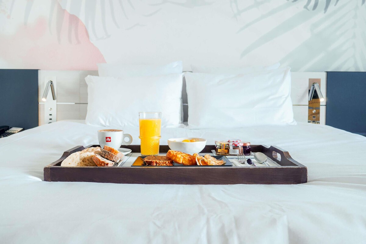 A neatly made breakfast tray on a bed with a white bedspread, a glass of orange juice, a cup of coffee, and various pastries.