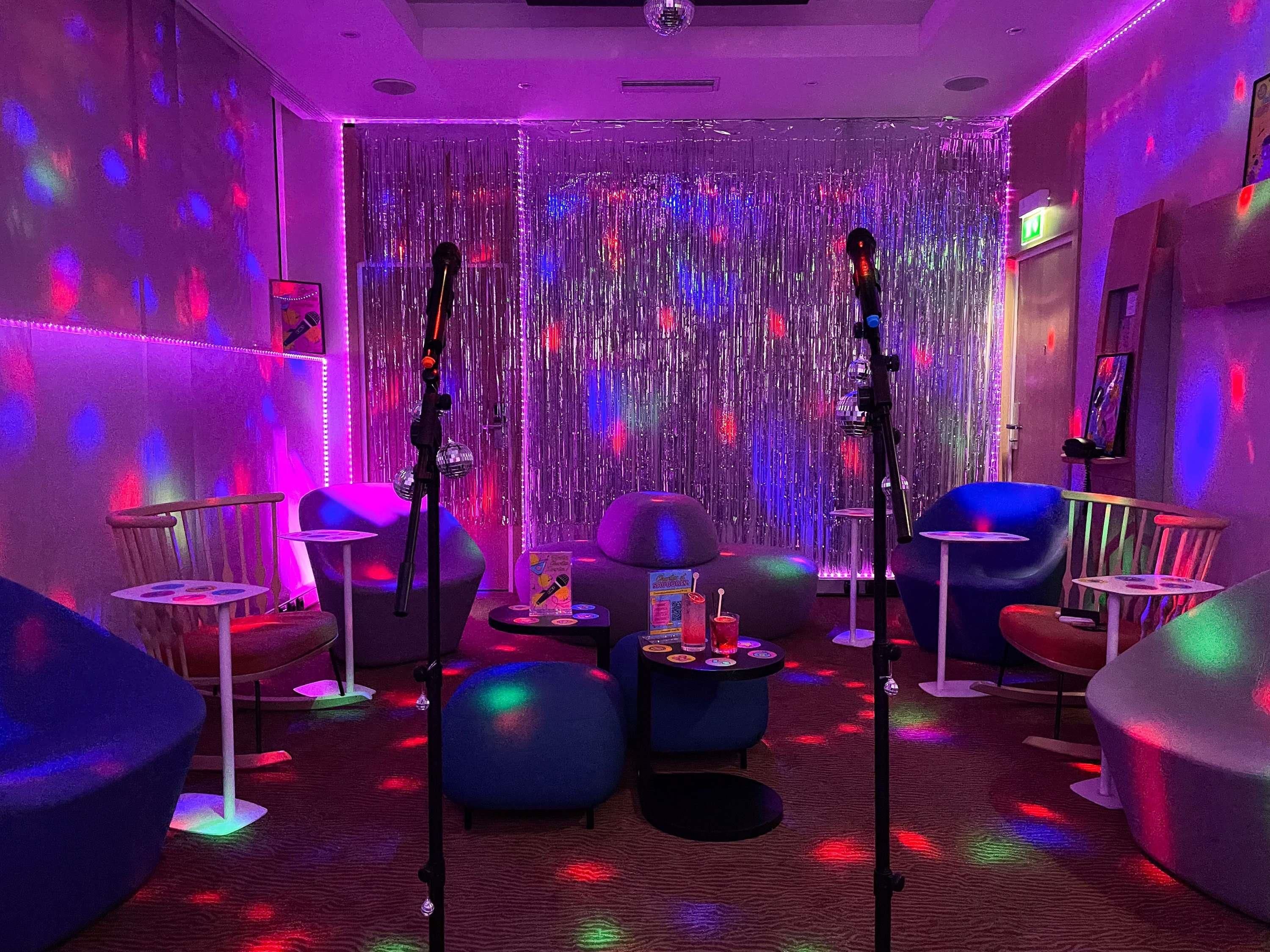 A room with a mirrored wall, two microphones, and a small table with a drink and a box.