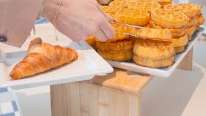 Montaje de buffet con gofres, un croissant y varios productos envasados a la vista.