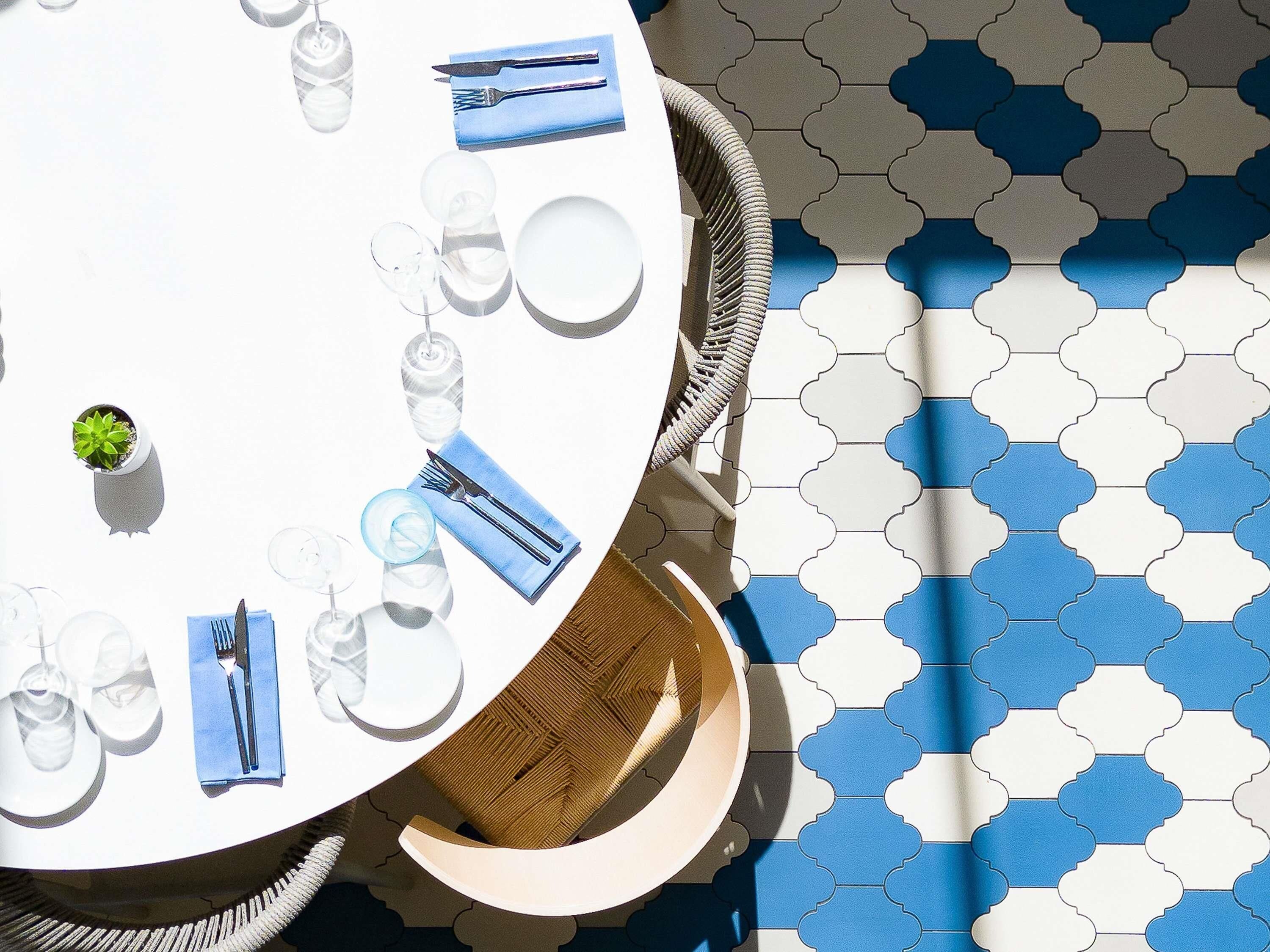 A round table with a white tablecloth, set with plates, glasses, cutlery, and a small potted plant.