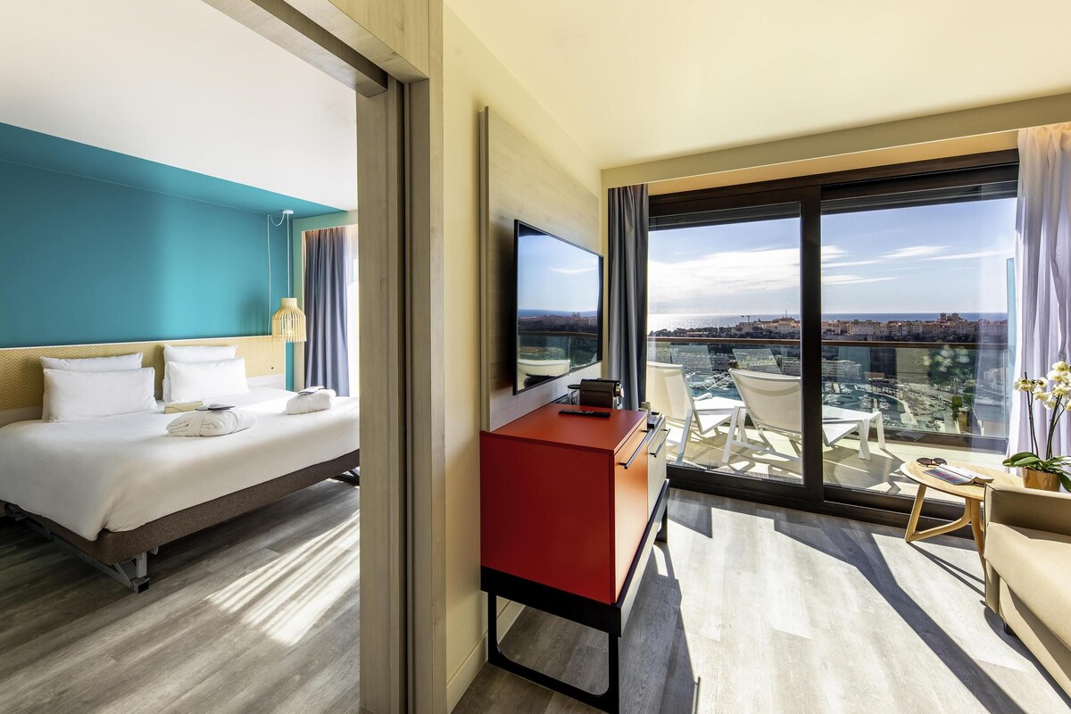 Une chambre d’hôtel moderne dotée d’un grand lit, d’un bureau et d’un balcon offrant une vue sur la ville.