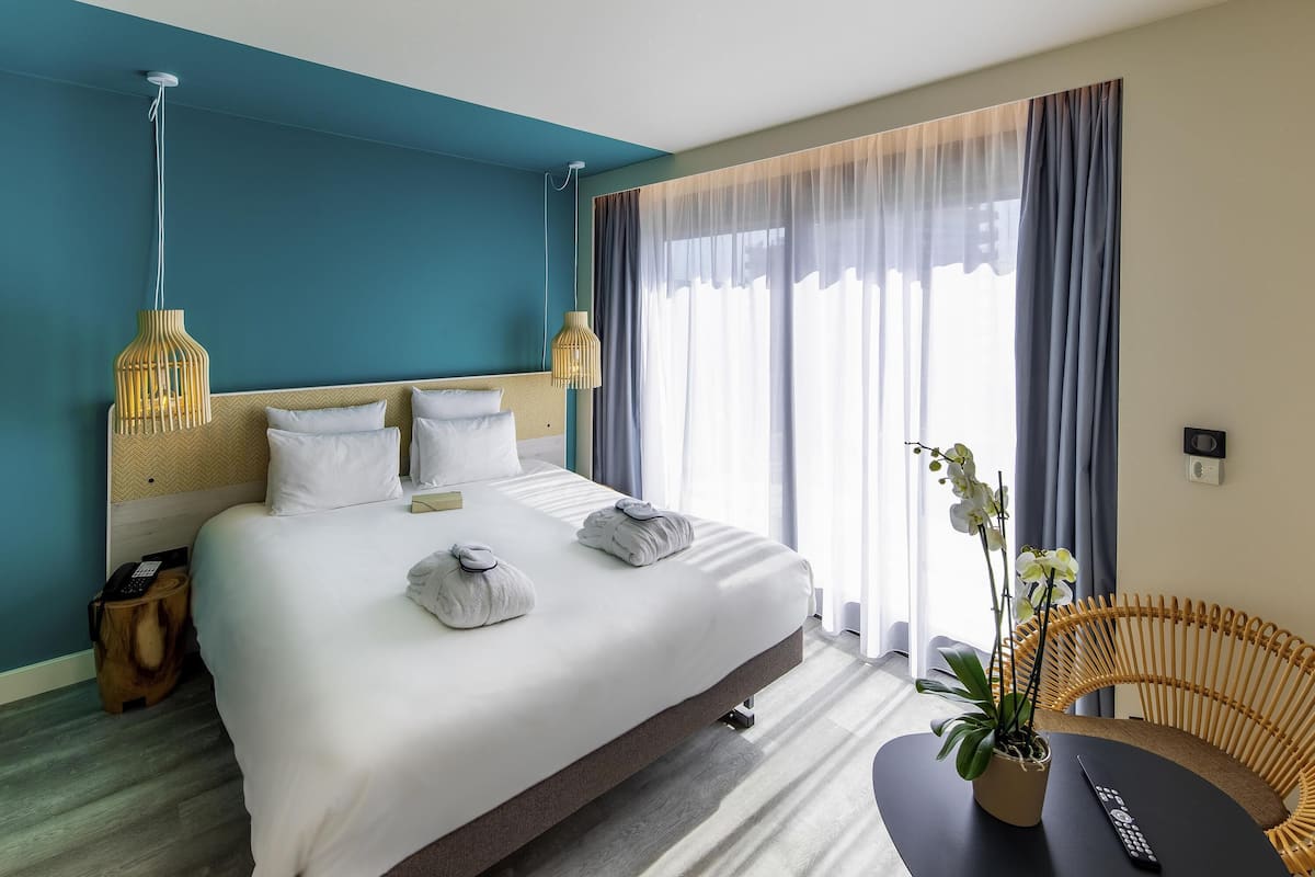 Ein Hotelzimmer mit einem großen Bett, Nachttischlampen, einem Nachttisch, einem Sessel und einer Topfpflanze.