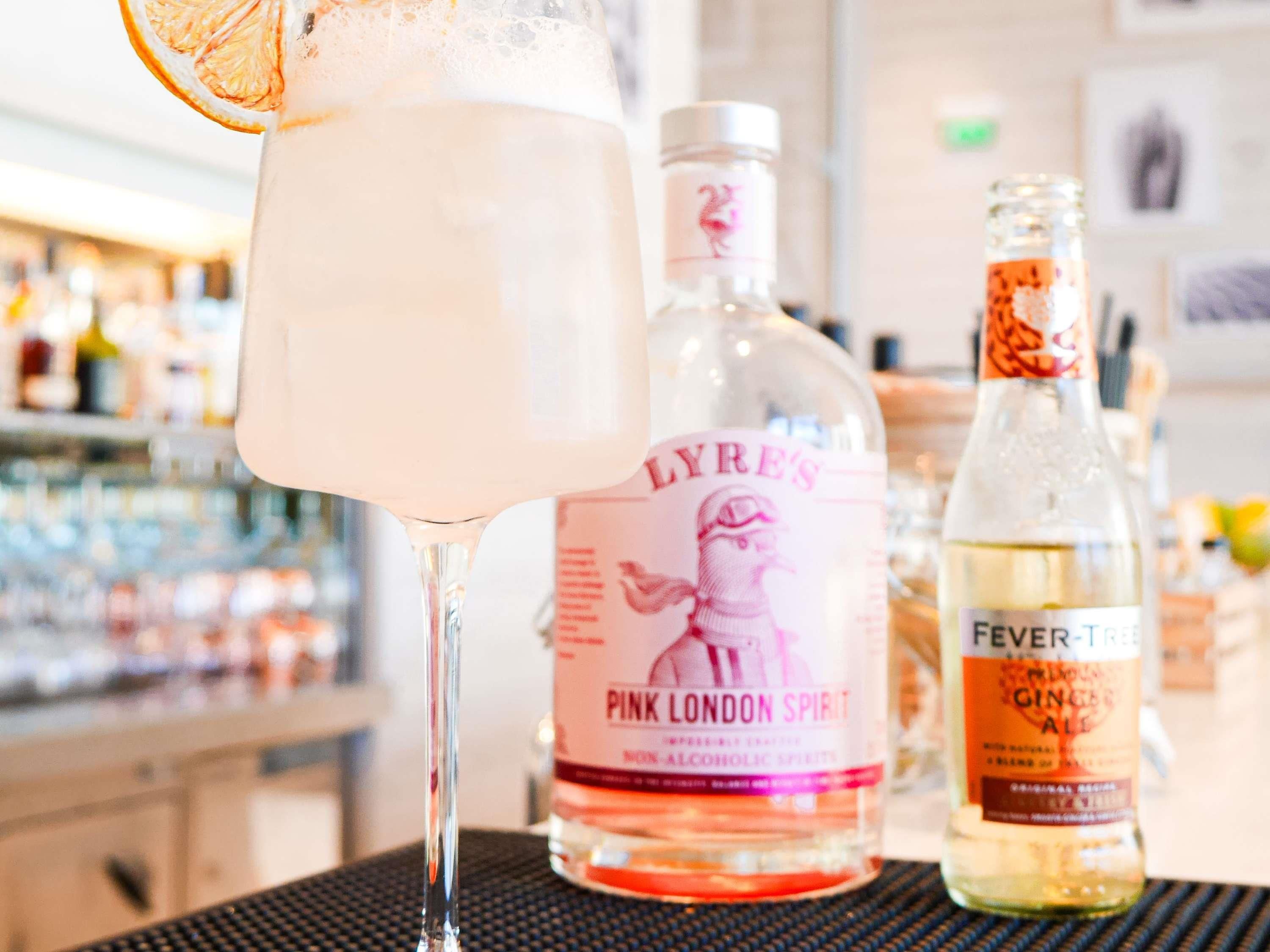 Un bar con una bebida en un vaso, una botella de Pink London Spirit y una botella de Fever Tree Ginger Ale.