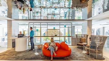 A modern lobby with a reception desk, a seating area with a large orange chair, and a unique ceiling design.