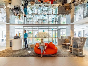 Un vestíbulo moderno con una recepción, un área de estar con un sillón naranja grande y un diseño de techo único.