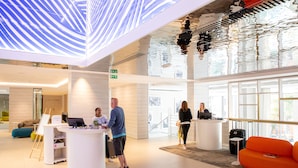 A modern lobby with a reception desk, seating areas, and a large glass wall.