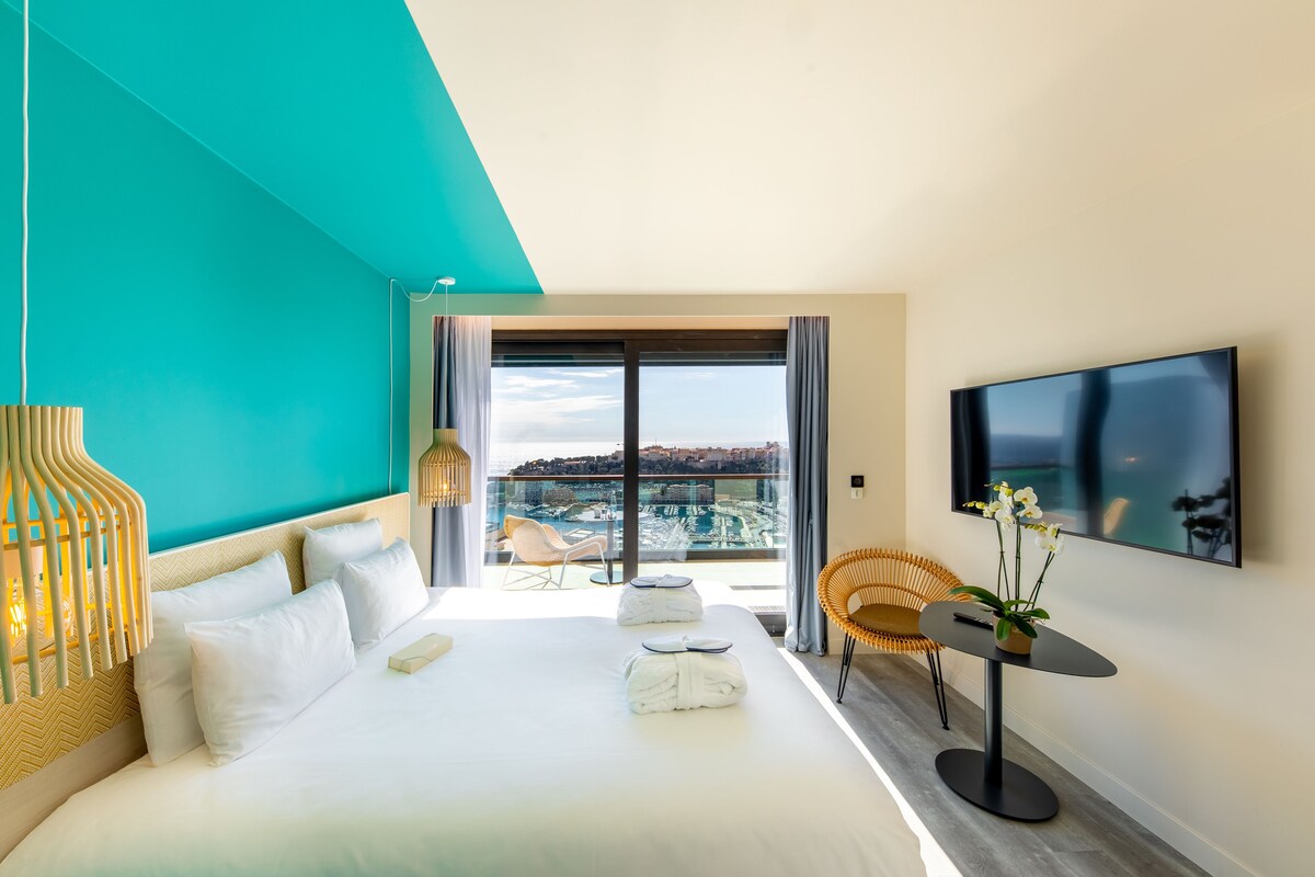 Een moderne hotelkamer met een groot bed, een balkon met uitzicht, een televisie en een klein tafeltje met een plant.