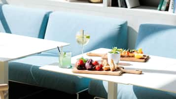Comedor con una mesa dispuesta para dos personas, que incluye una bebida, una bandeja de frutas y una pequeña planta.