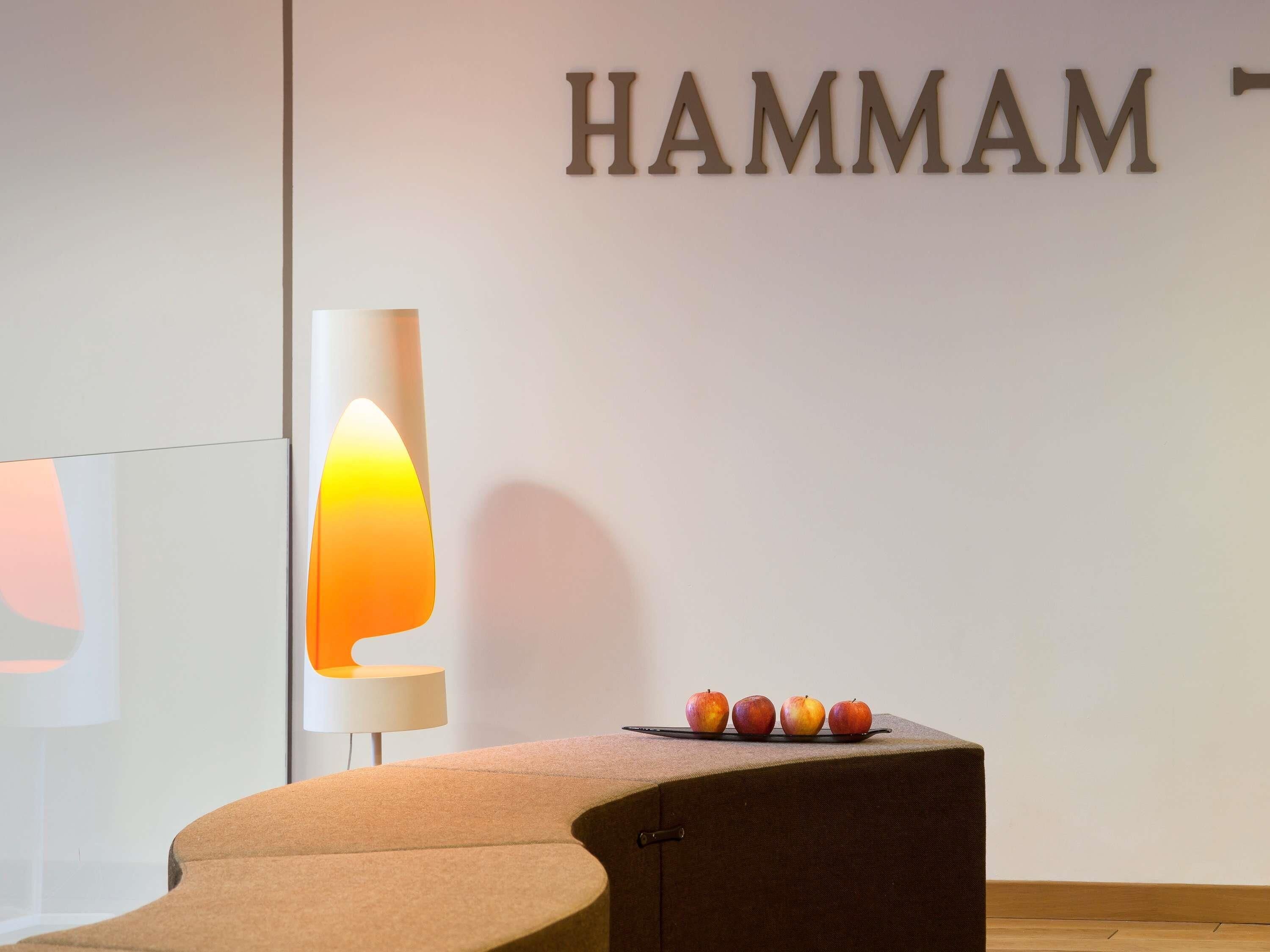 A modern interior with a wall-mounted sign reading "HAMMAM" and a curved seating area with a small table holding three apples.