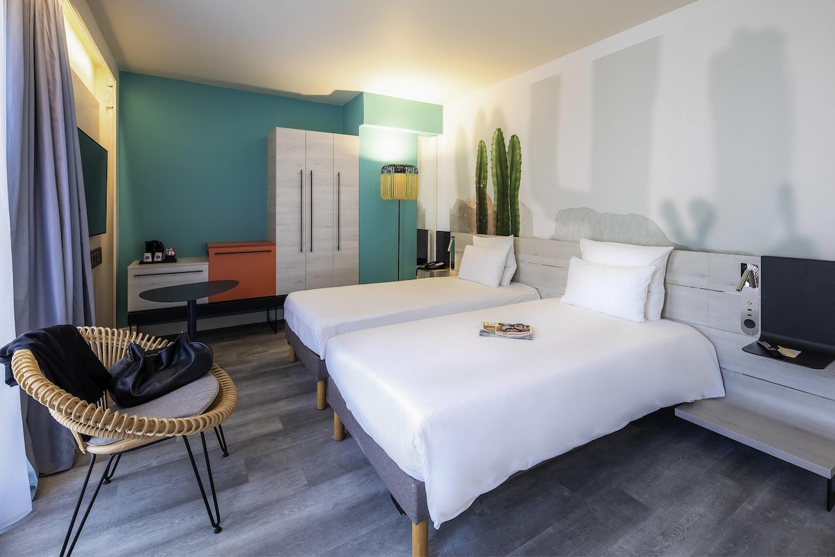 A hotel room with two beds, a desk, a chair, a wardrobe, and a TV.