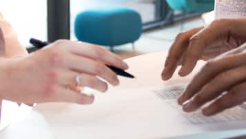 A close-up of hands signing a document at a counter with a pump bottle of hand sanitizer nearby.