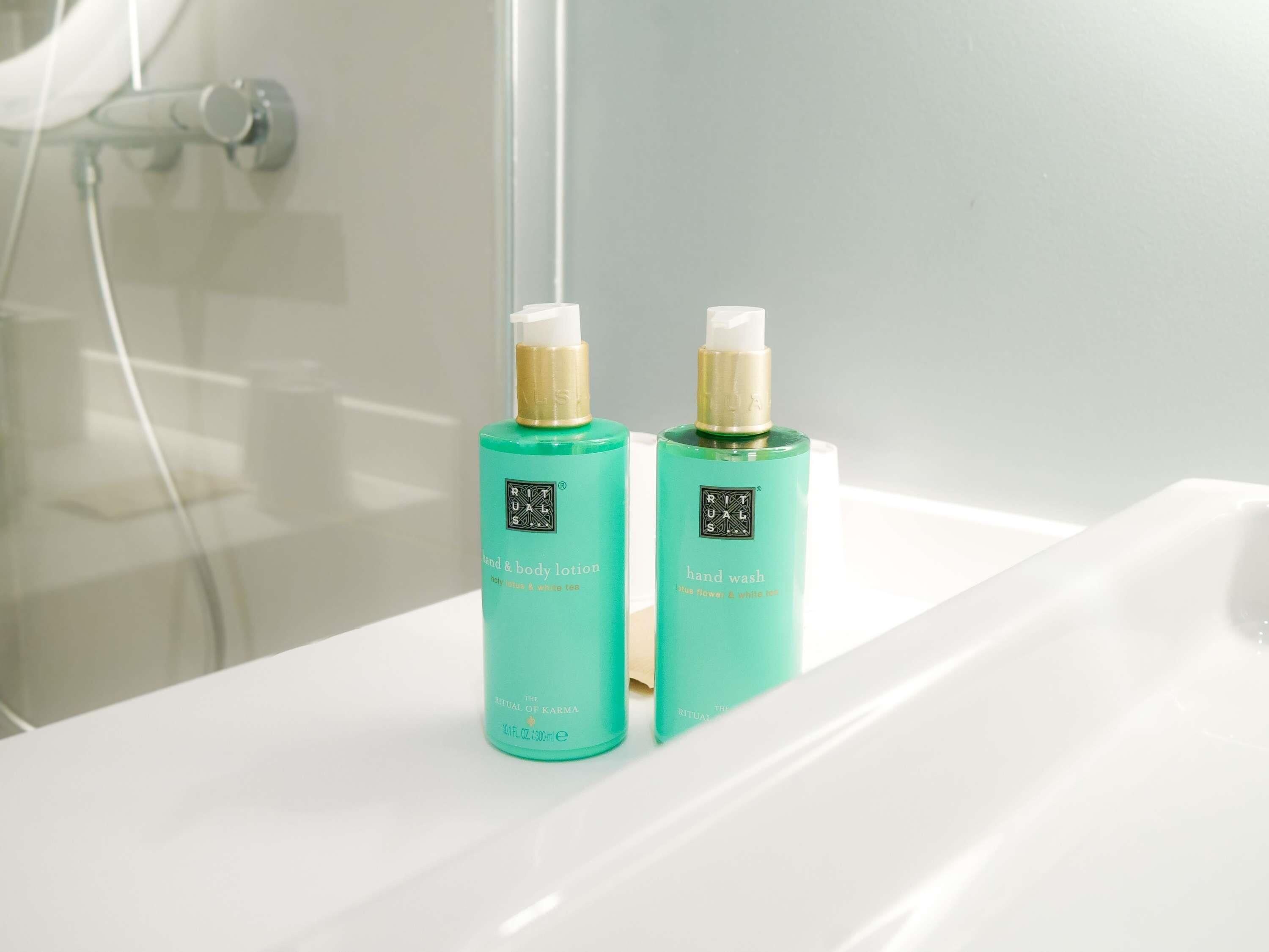 Two bottles of hand and body lotion on a white bathroom sink.