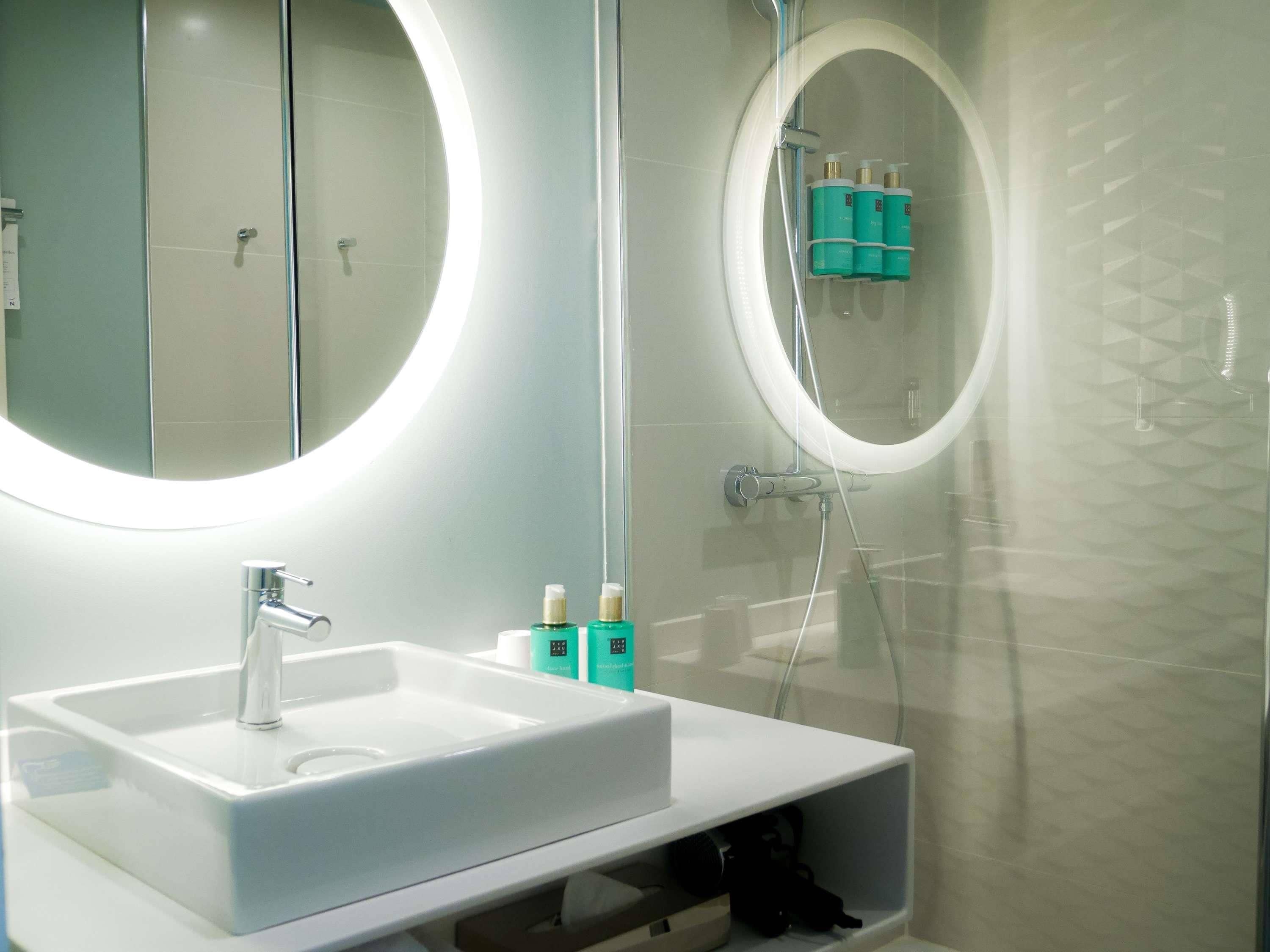 Une salle de bain moderne avec un lavabo blanc, un grand miroir et un espace douche.