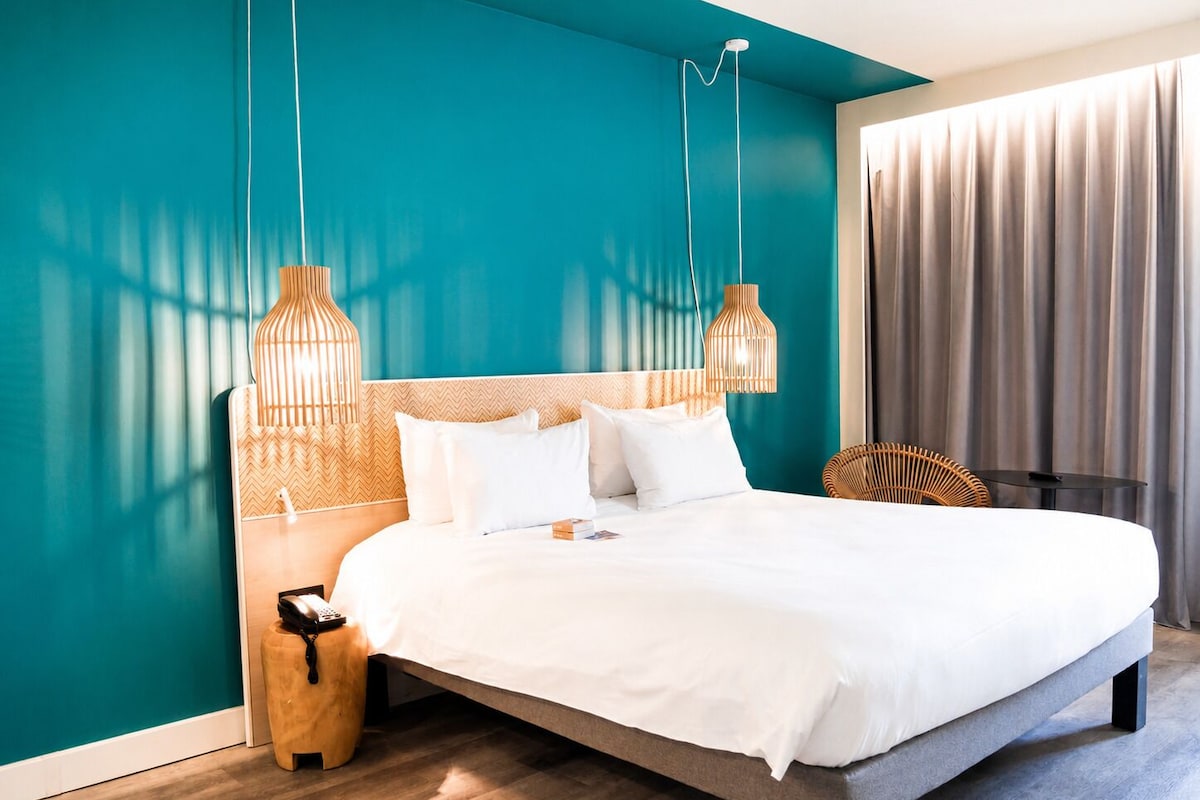 Een moderne hotelkamer met een groot bed, teal muren en een houten vloer.