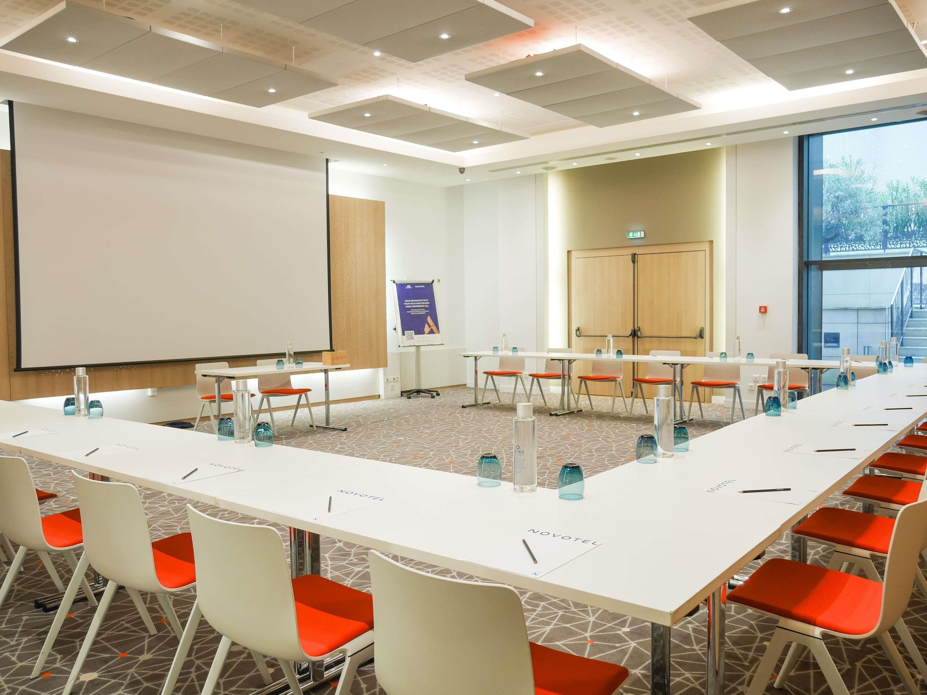 A conference room with a long table, white chairs, and a projector screen.