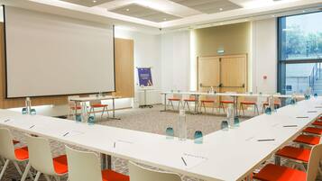 A conference room with a long table, white chairs, and a projector screen.