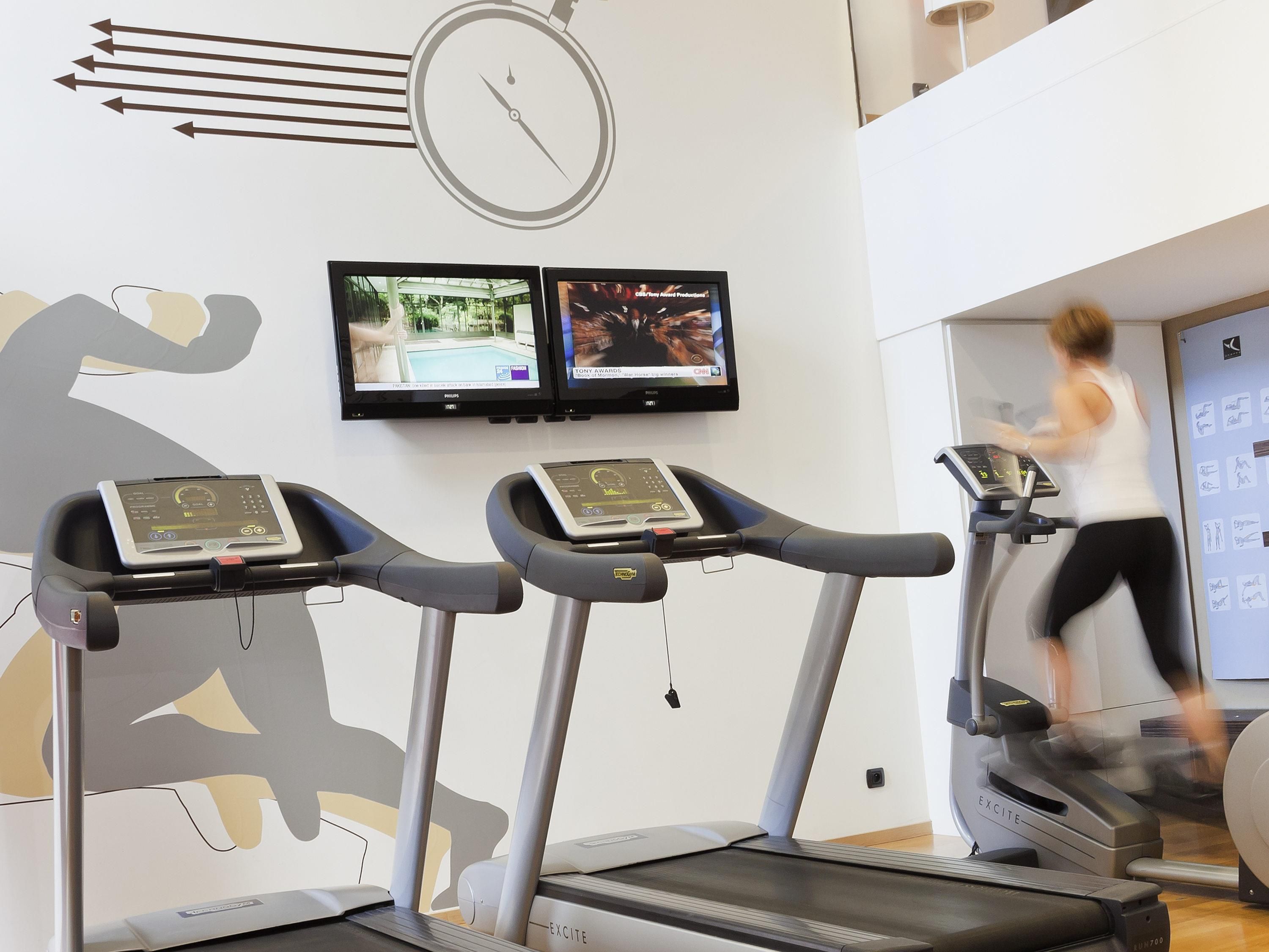 A gym with treadmills, a wall clock, and two TVs displaying sports content.