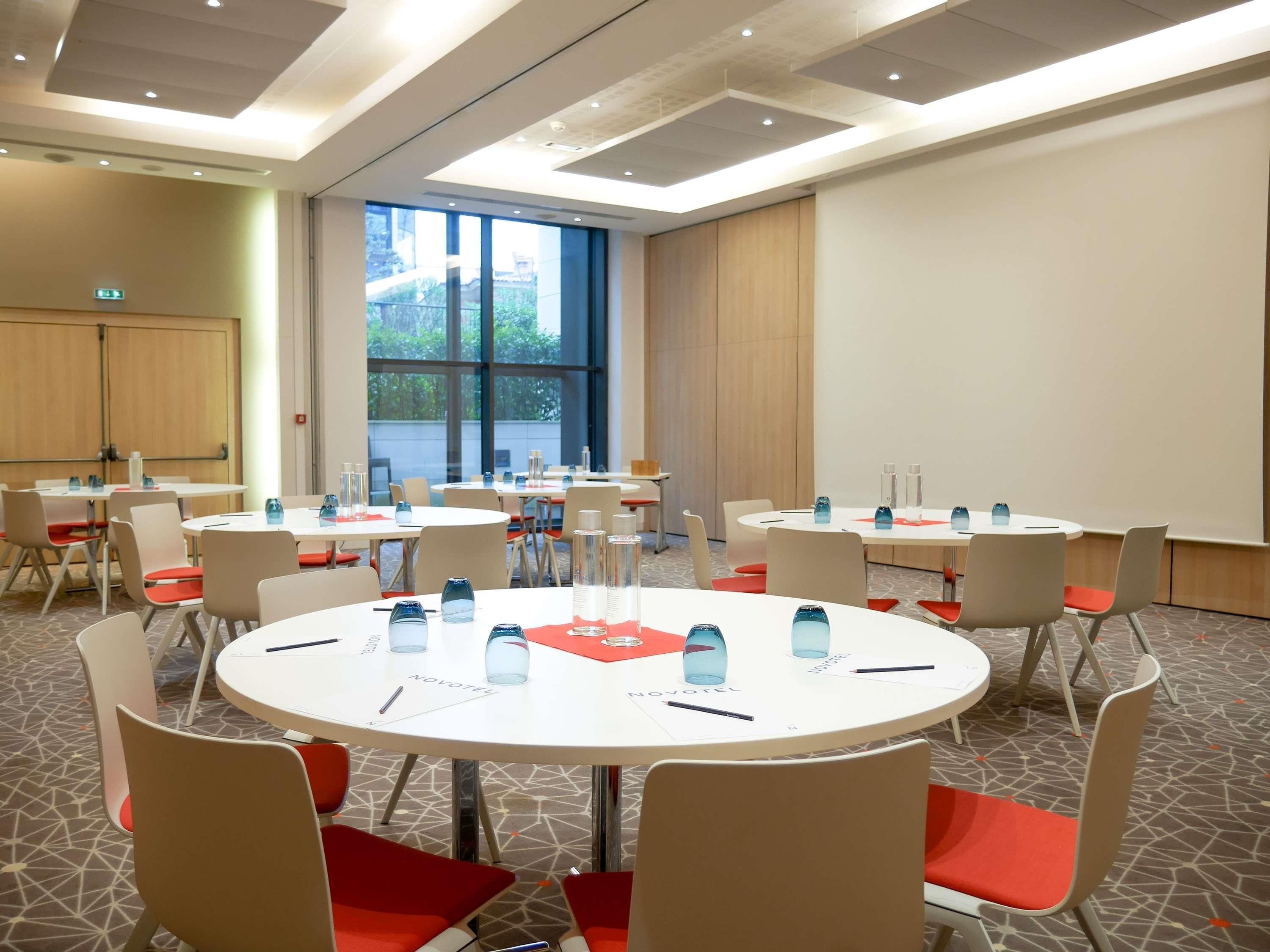 Sala de conferências com mesas redondas, cadeiras e garrafas de água.