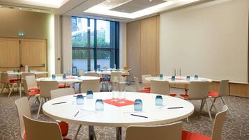 Sala de conferências com mesas redondas, cadeiras e garrafas de água.