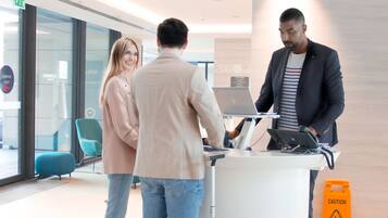 Een receptiebalie met een laptop, een blauwe koffer en een waarschuwingsbord.