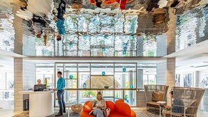 Un vestíbulo moderno con una recepción, un área de estar con un sillón naranja grande y un diseño de techo único.